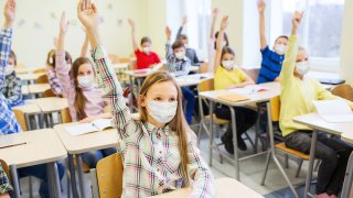 estudiantes alzando la mano con mascarillas puestas.