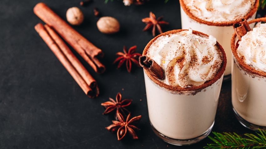 Traditional Christmas drink Eggnog with whipped cream and cinnamon on dark stone background. Hot beverage for winter holidays.