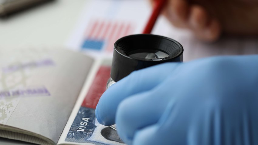 Specialist with loupe checking authenticity of american visa in passport close-up