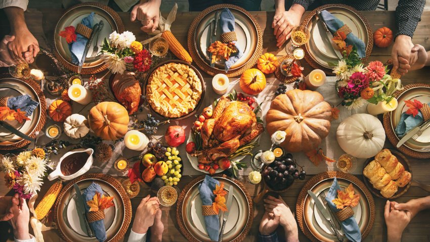 Group of friends or family members giving thanks to God at festive turkey dinner table together. Thanksgiving celebration traditional dinner concept