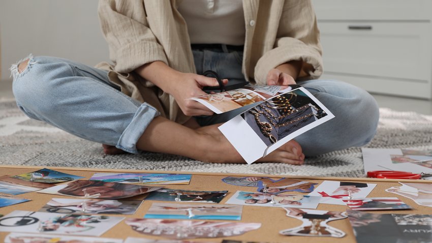 Creating vision board. Woman cutting out picture on floor indoors, closeup