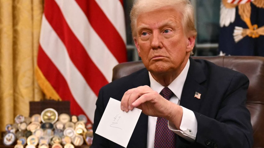 US President Donald Trump holds up outgoing President Joe Biden’s letter as he signs executive orders in the Oval Office of the WHite House in Washington, DC, on Jan. 20, 2025.