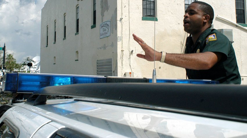 PUNTA GORDA, FL – AUGUST 14:  Lt. Stefan Blue, with Florida Bureau of Investigative Services, talks to drivers after Hurricane Charley struck southwest and central Florida August 14, 2004 near downtown Punta Gorda, Florida. The roof on the building in background was blown off. Officials in Florida said at least 15 people were killed and many more were unaccounted for after Hurricane Charley left a path of destruction across Florida then continued north and struck the Carolinas.  (Photo by Tim Boyles/Getty Images)