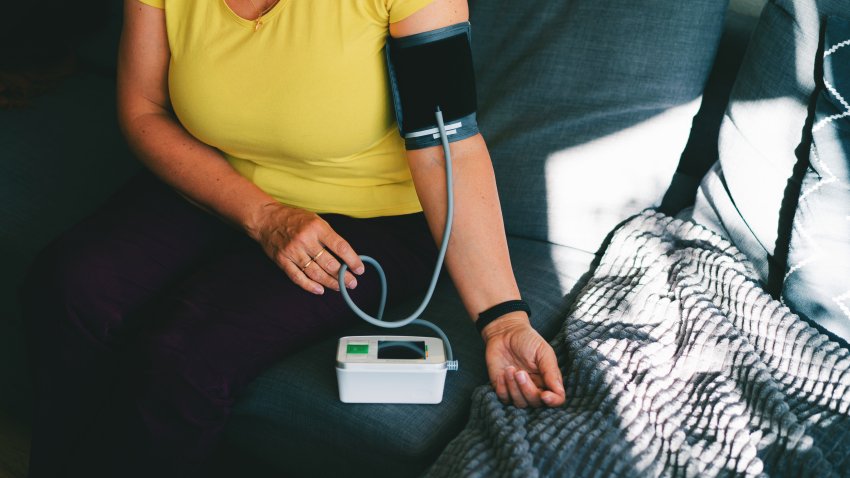 A close-up image of a person checking their blood pressure at home using a digital blood pressure monitor. The scene shows a relaxed individual seated on a cozy couch with a blood pressure cuff on their arm, illustrating the ease and convenience of home health monitoring. This image is ideal for conveying themes of health awareness, self-care, or medical technology in everyday life.